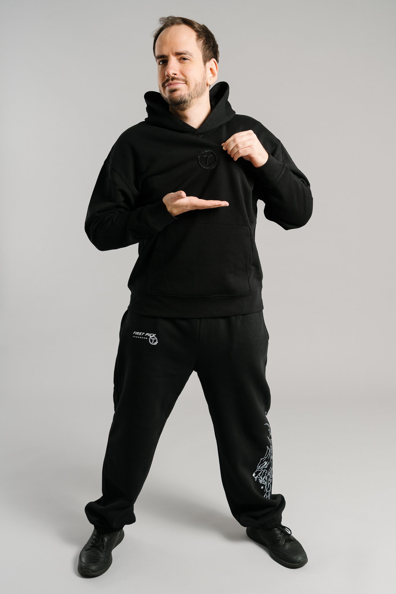 Schwarzer Hoodie aus weichem Sweatstoff mit dezentem Ton-in-Ton-Sticklogo auf der Brust. Das schlichte Design mit Kapuze und Kängurutasche wirkt modern und sportlich. Der Hoodie wird in voller Ansicht gezeigt und betont den minimalistischen, cleanen Look der Streetwear-Kollektion.