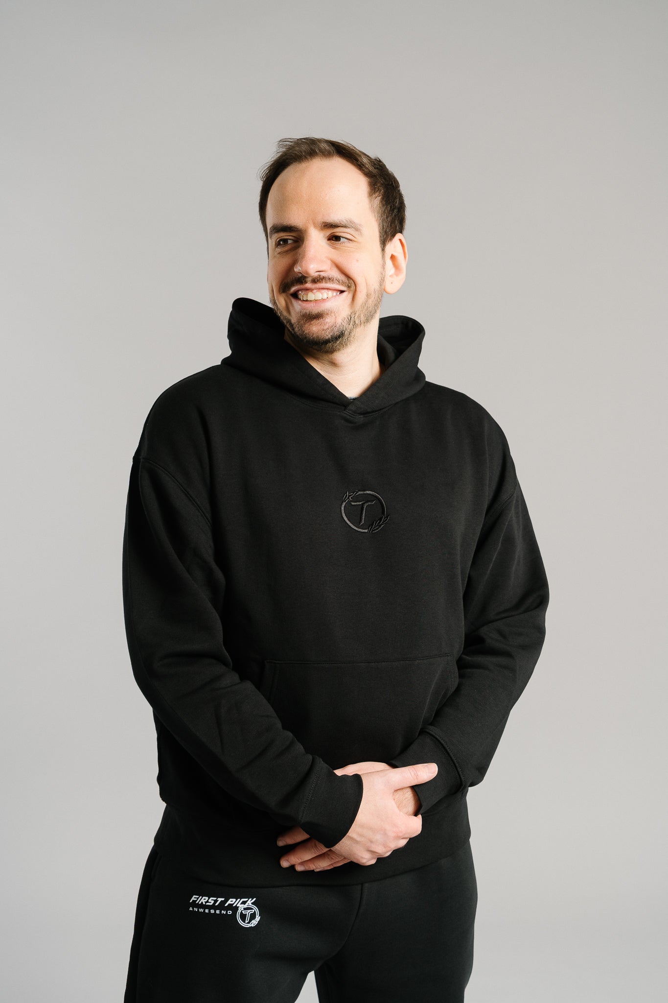 Schwarzer Hoodie aus weichem Baumwollstoff mit dezenter Ton-in-Ton-Stickerei eines stilisierten „T“ im Lorbeerkranz auf der Brust. Das Design ist schlicht, modern und hochwertig verarbeitet, mit klassischer Kängurutasche und Kapuze. Der Pullover steht für einen cleanen Streetwear-Look mit sportlicher Note.