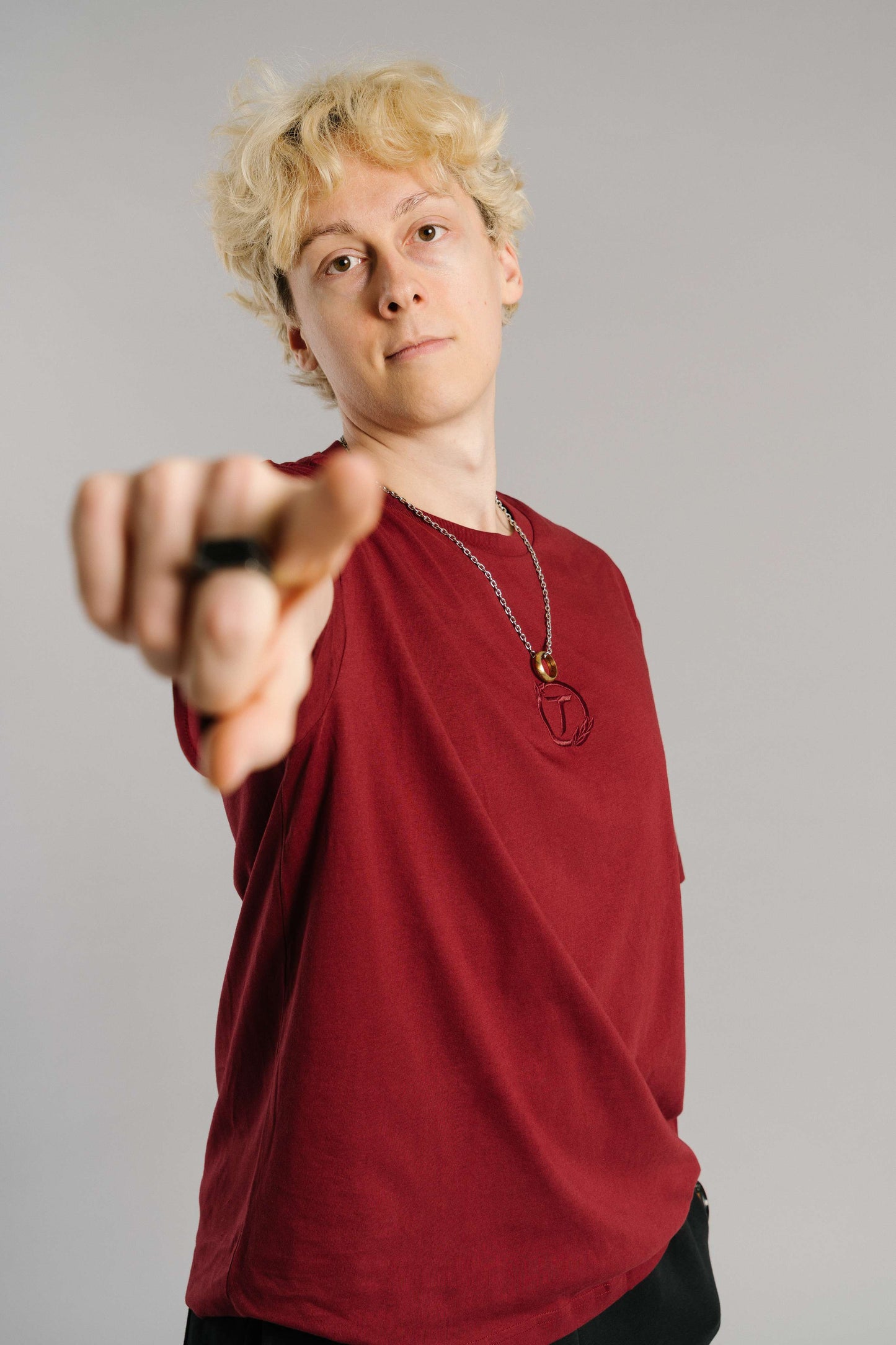 Ein burgunderrotes T-Shirt mit tonaler Stickerei des „T“-Logos im Lorbeerkranz auf der Brust. Das Shirt hat einen lockeren Schnitt mit kurzen Ärmeln und einem klassischen Rundhalsausschnitt. Der Fokus liegt auf der Brustpartie mit der dezenten Logo-Stickerei.