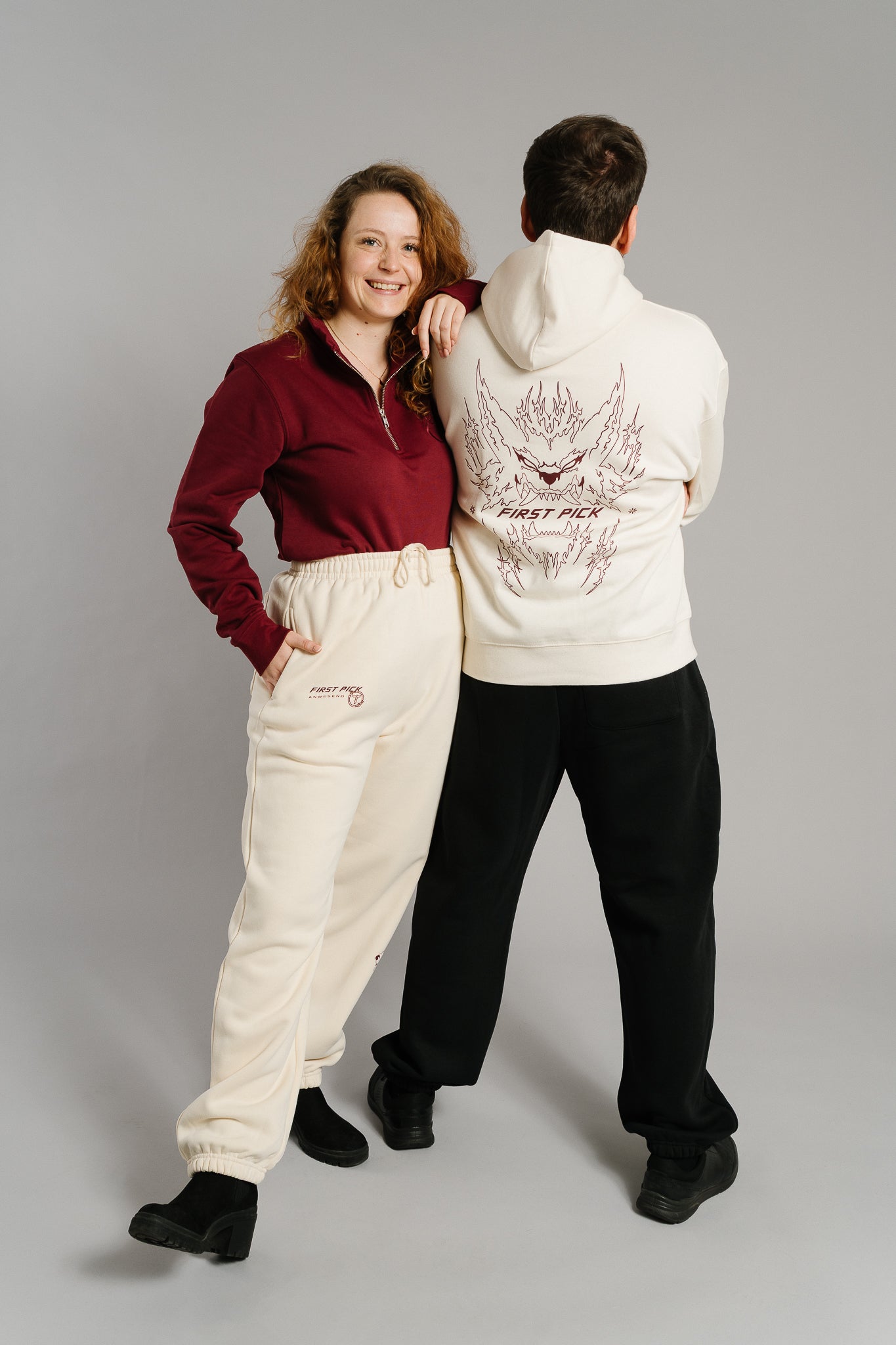 Beigefarbene Jogginghose mit lockerer Passform und elastischen Bündchen an Bund und Knöcheln. Auf der linken Vorderseite befindet sich ein braunroter Aufdruck mit der Aufschrift „FIRST PICK ANWESEND“ und einem runden Logo. Die Hose besteht aus weichem Sweatstoff und hat seitliche Eingrifftaschen.