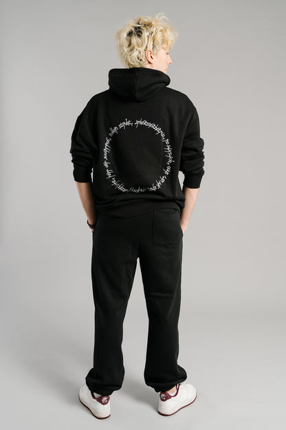 Schwarzer Hoodie mit großem weißen Schriftzug-Print auf der Rückenpartie. Das Design zeigt einen kreisförmig angeordneten Text in handschriftlicher Typografie. Der Kapuzenpullover besteht aus weichem Material, hat eine lockere Passform und betont durch das schlichte Schwarz-Weiß-Kontrastdesign einen modernen Streetwear-Look.