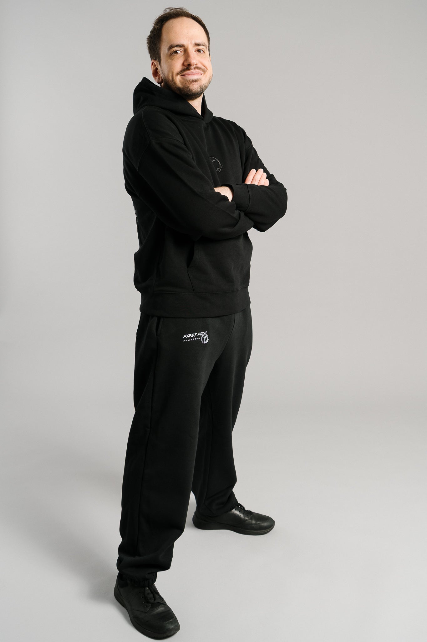 Schwarze Jogginghose aus weichem Sweatstoff mit geradem Schnitt und elastischen Bündchen an den Knöcheln. Auf dem linken Oberschenkel ist ein weißer Schriftzug „FIRST PICK ANWESEND“ mit rundem Logo platziert. Die Hose wirkt gemütlich und hochwertig verarbeitet – ideal für Streetwear- oder Freizeit-Looks.