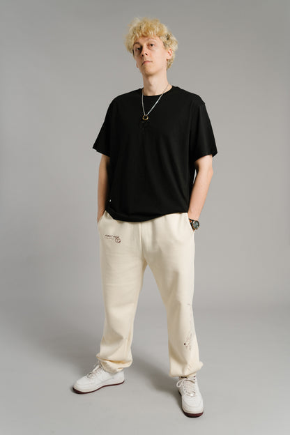 Schwarzes T-Shirt mit dezentem, schwarzem Sticklogo auf der Brust. Das Logo zeigt ein stilisiertes „T“ in einem Lorbeerkranz. Das Shirt hat einen lockeren, geraden Schnitt mit weichen Baumwollfasern und vermittelt einen minimalistischen Streetwear-Look.