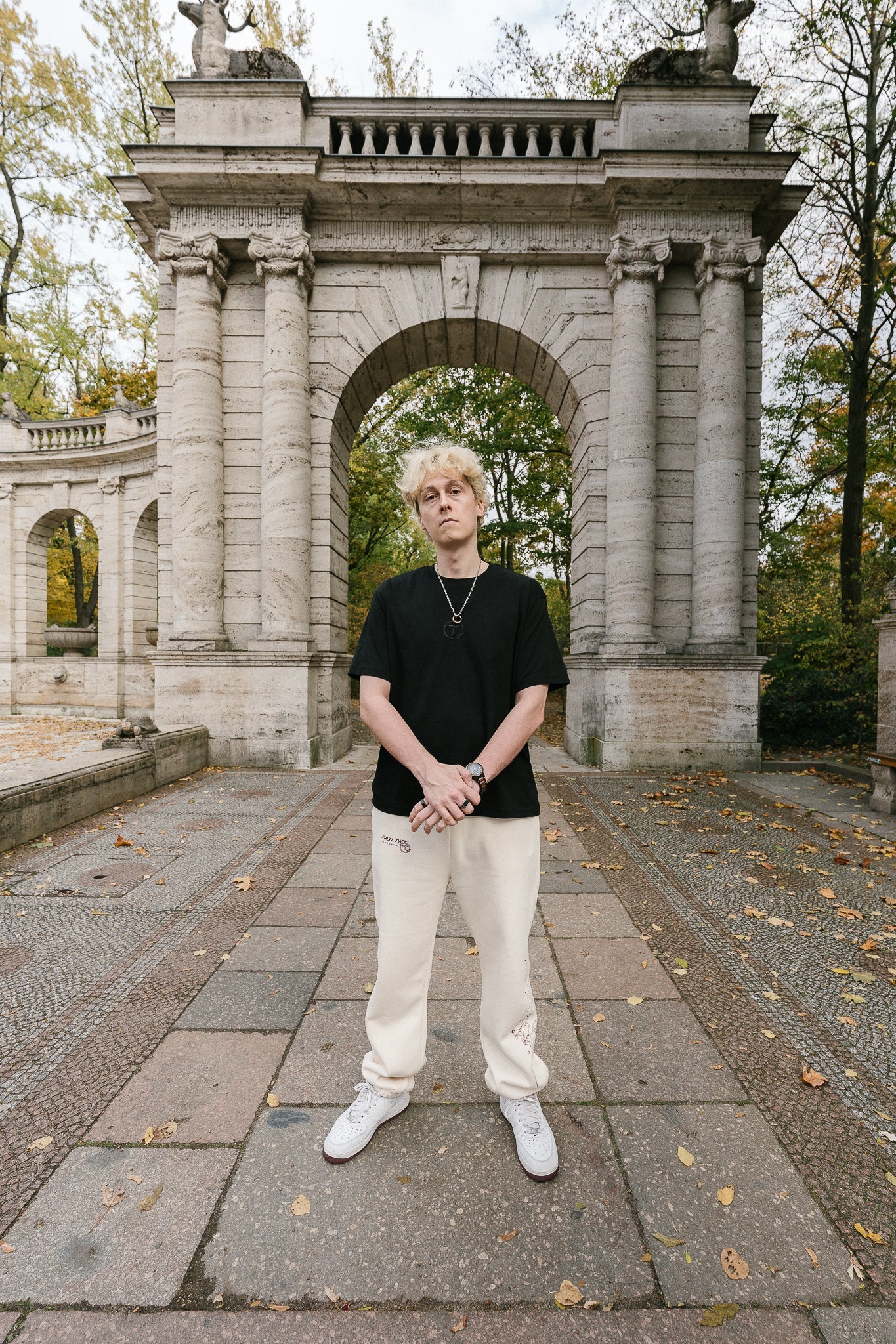 Schwarzes T-Shirt aus weicher Baumwolle mit gesticktem Ton-in-Ton-Logo auf der Brust. Das Design zeigt ein stilisiertes „T“ im Kreis mit Lorbeerzweigen. Das Shirt hat einen lockeren Schnitt und vermittelt einen cleanen, modernen Streetwear-Look, kombiniert mit heller Hose und sportiven Sneakern.