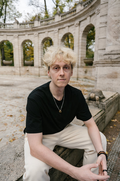 Schwarzes T-Shirt mit dezentem Ton-in-Ton-Sticklogo auf der Brust. Das Logo zeigt ein stilisiertes „T“ in einem Lorbeerkranz. Das Shirt besteht aus weicher Baumwolle, hat einen geraden, entspannten Schnitt und verkörpert einen modernen Streetwear-Look in minimalistischer Gestaltung.